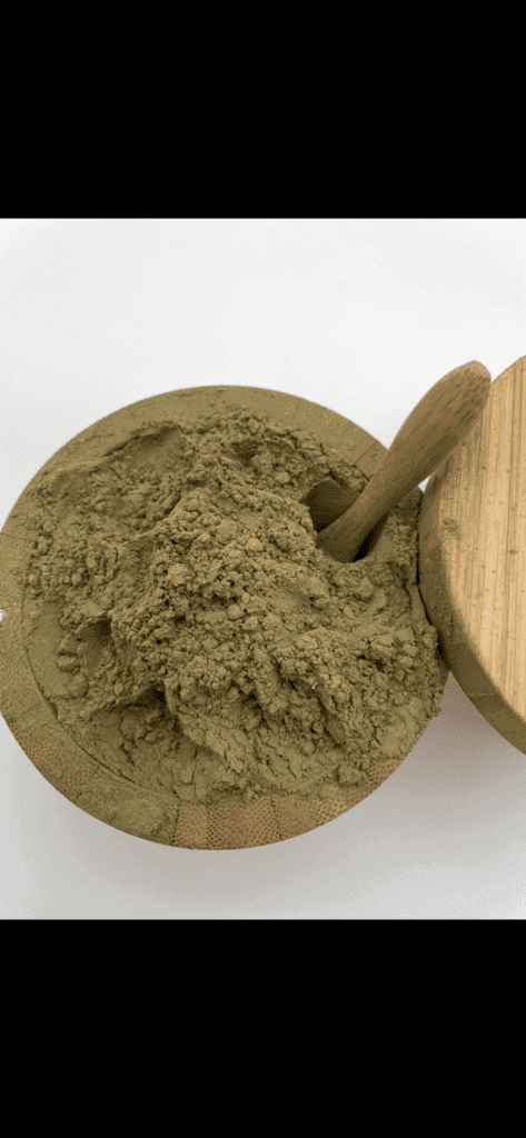 A bamboo bowl heaped with green kratom powder with a wooden scoop resting in it