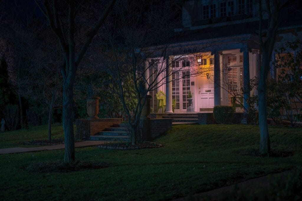 A detached house with a lit front porch and glowing windows in the evening, framed by bare trees