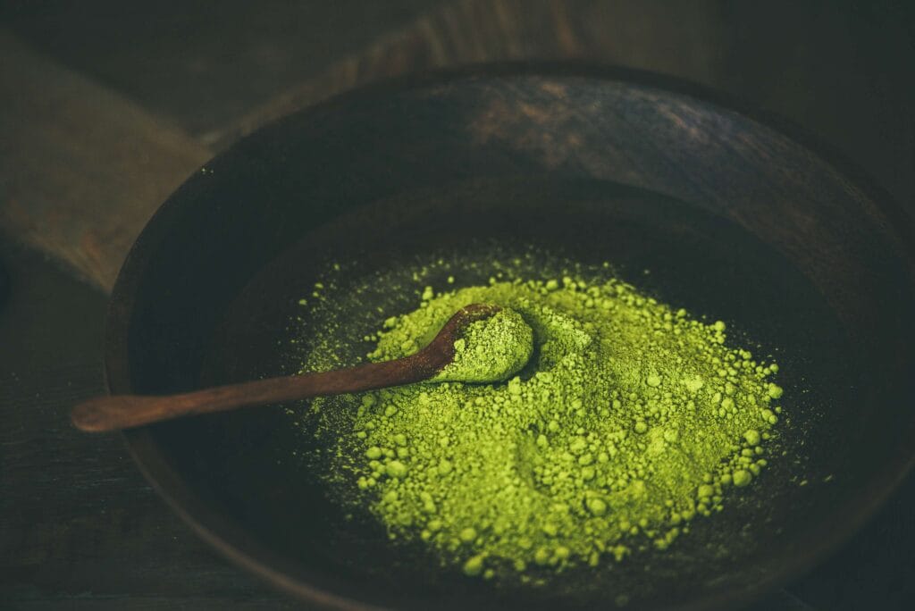 Bright green kratom powder with a wooden scoop drawn through it, seen from directly above