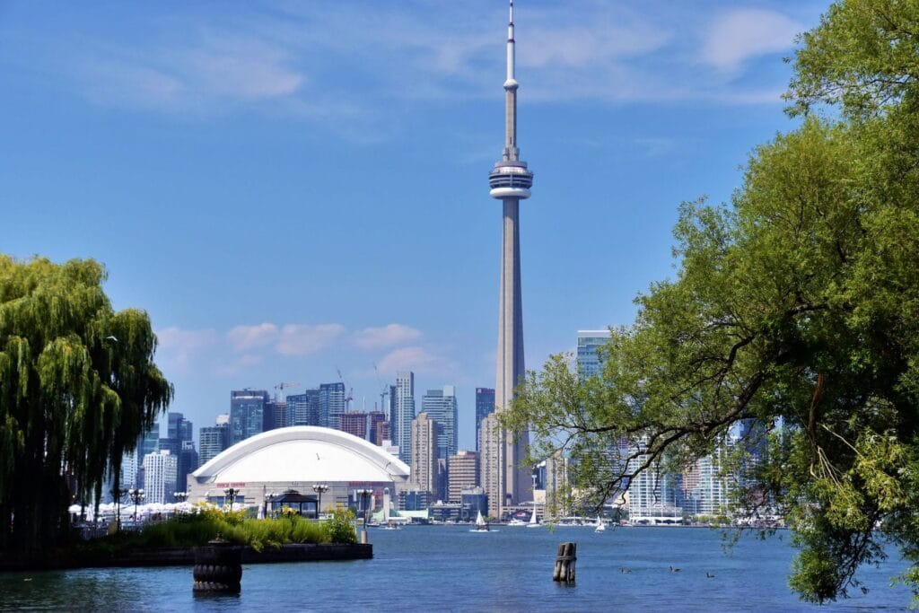The Toronto skyline and CN Tower seen across the water, framed by trees on the near shore