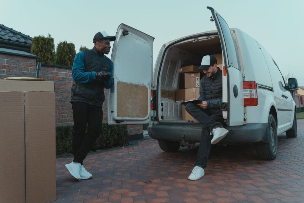 Two delivery workers loading boxes into an unmarked white van on a residential driveway