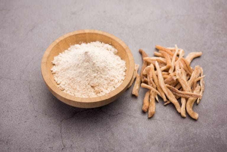 Ashwagandha root pieces beside a wooden bowl of ashwagandha powder