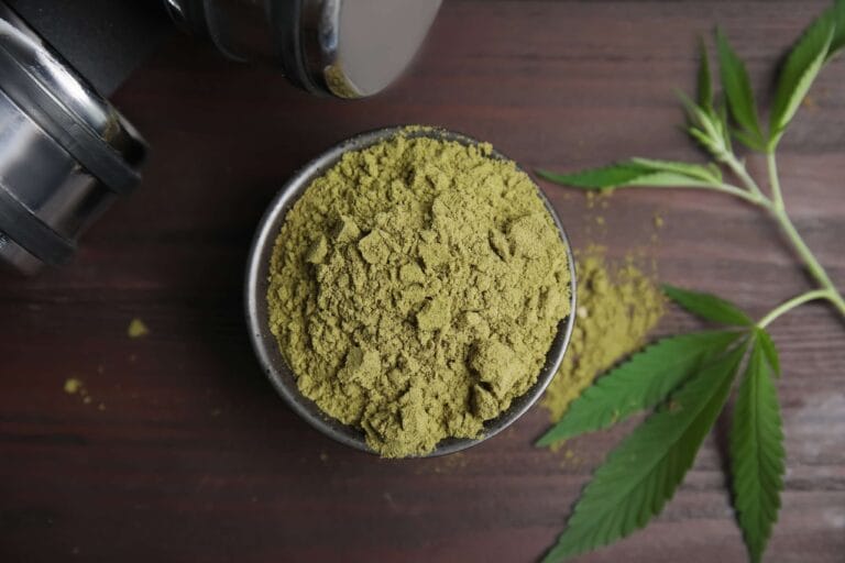 Green botanical powder in a wooden bowl beside a potted plant